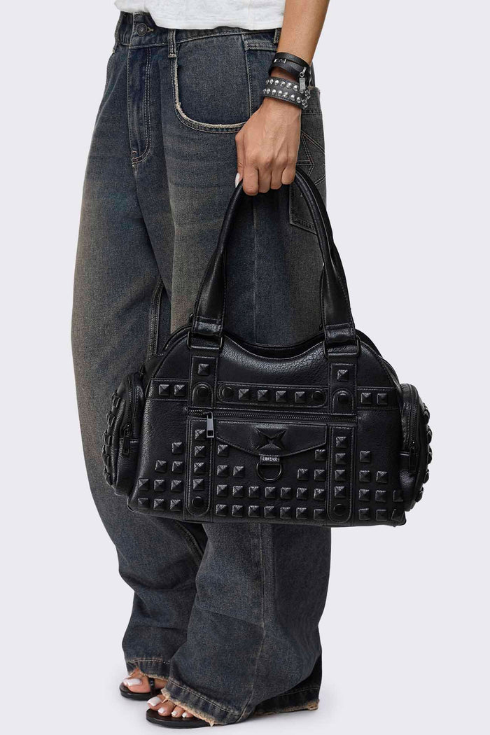 Black faux leather shoulder bag with pyramid studs, front zip pocket, side pockets and two top handles.