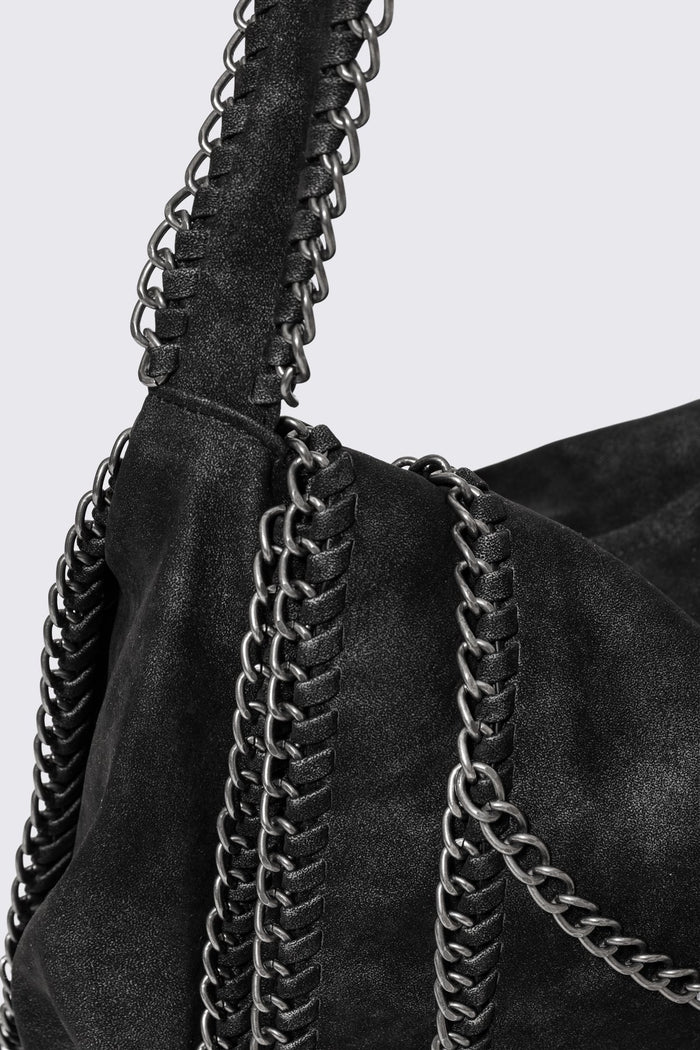 Black faux suede shoulder bag with chain trim, layered chains and fold-over flap in a grunge Y2K style.
