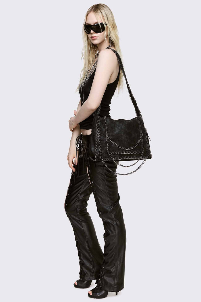 Black faux suede shoulder bag with chain trim, layered chains and fold-over flap in a grunge Y2K style.