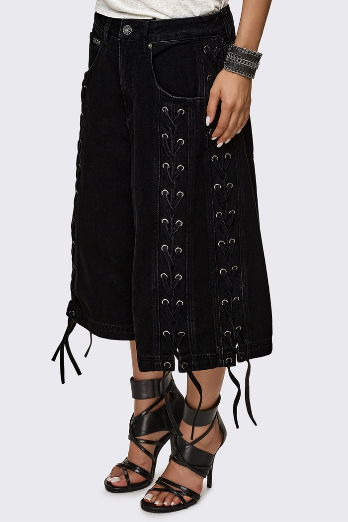 Black washed denim jorts with lace-up corset sides, baggy wide-leg fit and grunge aesthetic.